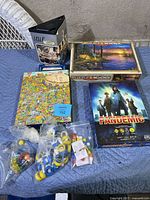 Lot overview showing board games, puzzles, and bags of assorted game pieces on blue surface