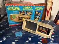 Fisher-Price Movie Viewer Theater device shown on a table next to its original box with water damage and wear.
