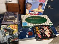Five vintage board games displayed on a table, including 'Murder She Wrote,' 'Top Secret,' Clue, Stockmarket, and Tac-Tic Turn.