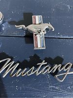 Photo showing full view of the Mustang leaping horse emblem on striped background and the Mustang signature emblem below it.