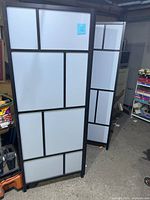 Front view of the 3-panel folding partition wall showing the geometric black framing and white opaque panels.