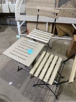 View showing two folding patio chairs with wooden slats and black metal folding frames alongside a beige plastic folding slatted top table