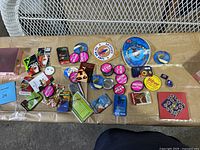 Top-down view of collection of pins spread on a table. Includes various circular and rectangular pins, some with event years and French text.