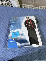 Front view of sealed costume packaging showing an adult male model wearing black priest robe, red stole with gold cross, brand Spirit, marked adult size one size fits most