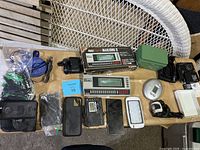 Overview of assorted items including boxed Mahjong II game console, phone cases, earbuds, small electronics, and accessories spread on table.