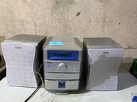 Front view of RCA mini stereo unit flanked by two RCA speakers on each side, placed on concrete surface.