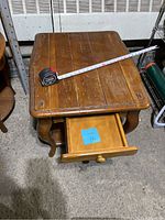 Rectangular wooden coffee table with tape measure showing length and drawer pulled open.