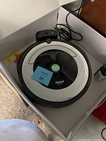 iRobot Roomba 690 robot vacuum powered on with CLEAN light on, placed inside white cardboard box with charging dock and power cable attached.