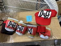 Image showing Duff Beer belt with multiple can holders and Duff logo, along with red Duff baseball cap.