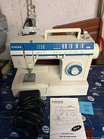 Singer HD110 sewing machine with power cord and instruction booklet on surface.