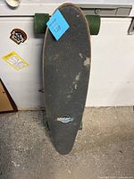 Top view of the skateboard showing black grip tape and wear marks, green wheels visible on sides.