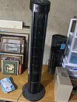 Full view of black Holmes tower fan standing on floor, showing tower shape and round base.