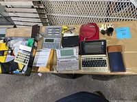 Full view of multiple calculators and electronic translators on a table including cases, power adapters, and a manual booklet.