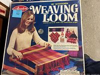 Box cover image showing Avalon brand 18-inch wooden weaving loom and woven sample of colorful fabric.