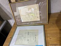 Two framed Asian calligraphy artworks displayed on a wooden surface, showing full view of both pieces.