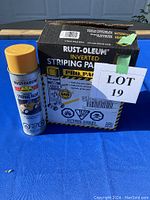 Closed box of Rust-Oleum inverted striping paint can beside one spray paint can with yellow cap, label showing usage for pavement line striping.