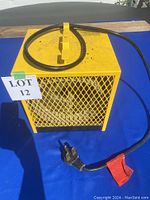 Full view of the yellow metal electric heater with protective mesh casing and attached power cord ending in an industrial plug.