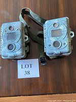 Two camouflage SpyPoint game cameras with straps placed on a wooden surface, showing their closed outer casings.