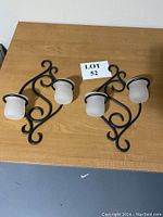 Pair of black wrought iron wall sconces each with two mounts for frosted glass candle holders on a wood table.