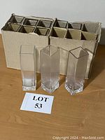 Three clear glass vases in front of cardboard box, showing rectangular and square shapes.