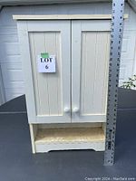 Front view of the white wooden medicine cabinet with two paneled doors and one open bottom shelf.