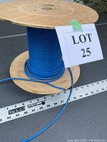Full view of a large wooden spool with blue Ethernet CAT 5 cable wrapped around it with a ruler for scale and a lot number card.