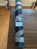 Rolled black metal mesh screen on a wooden surface, secured with tape, rolled tightly and labeled with lot number 51.