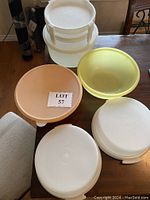 Five assorted Tupperware kitchen items arranged on a table: three white pie platters with lids stacked and two mixing bowls in yellow and peach colors.