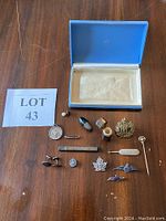 Photo showing assortment of vintage pins, cufflinks, and a blue jewelry storage box on wooden surface.
