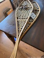 Two vintage wooden snowshoes stacked on a wooden table with a lot tag 36 visible.