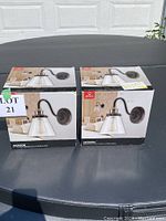 Two boxed new Jackson wall sconce lights by Globe showing product packaging with bronze finish and clear glass shades.