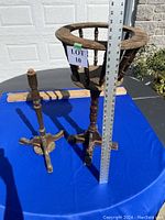 Full view of round wooden planter stand with spindles and tripod legs, tape measure for scale showing about 28 inches tall, visible broken detached leg piece behind.