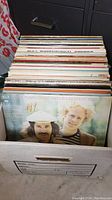 Photo of approximately 70 vinyl albums stored in a cardboard box, showing Simon and Garfunkel Greatest Hits album on top.