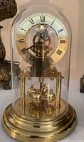 Front view of Birks Quartz Anniversary Clock with glass dome in place, showing Roman numeral clock face and brass rotating pendulum inside glass dome on brass base.
