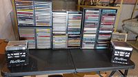 Full view of multiple CD racks fully loaded with CDs, two Kool Krates plastic crates filled with CDs in front on a folding table.
