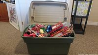 Photo of the green Rubbermaid tote with hinged lid containing various Christmas wrapping supplies including wrapping paper, bows, and ribbons.