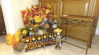 Full view of the fall decor set including the candle centerpiece, twig swans, faux flower arrangements, decorative bottle, and small metal table.
