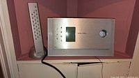 Front view of Grundig Ovation stereo system with remote control beside it, silver finish, illuminated display.