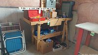 Wooden workbench with storage drawers and shelves containing various hand tools and hardware including blue folding chairs on the side.