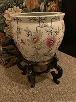 Front view of the ceramic planter showing floral patterns and detailed wooden stand