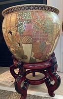 Front side of large koi pot with raised relief design and part of wooden stand visible