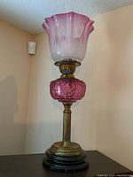 Full view showing black marble base, brass column, cranberry glass font, and fluted ombre pink-to-white etched glass shade