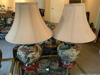Full view of the pair of lamps showing ceramic bases, wooden feet, and large flared cream shades on a glass table.