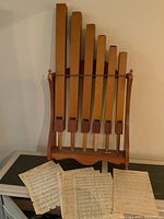 Full view of wooden wind instrument set mounted on wooden stand with printed music sheets spread in front, showing condition and extent of the instruments.
