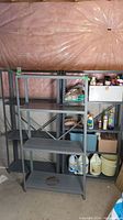View of three metal shelving units with various dimensions, against a wall with pink insulation. Two taller units measure 30x12x59 inches, one shorter unit measures 30x12x57 inches. Shelves are dark gray metal with cross back braces.