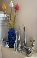 Full view of the Mid Century decor items including the Royal Copenhagen vase filled with decorative wooden flowers, four sleek polished metal geese sculptures, and the Pumper Jack reindeer figurine.