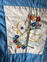 Close up of embroidery showing duck with floral embroidery on blue and white fabric