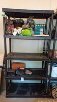 Full view of black plastic shelving unit with items placed on shelves as reference, unit shows size and condition needing cleaning.