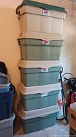 Five stacked Rubbermaid Rough Totes with green lids and beige or green bases in a garage or storage area.