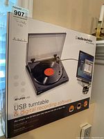 Photo of the box showing the Audio-Technica AT-LP2D-USB USB turntable with a vinyl record on the platter and clear dust cover.